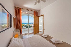 A hotel room with a bed, a bedside table with a lamp, a view of the sea, and a balcony with curtains. - Rouladina Apt 3 (Stalos)