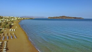 Une plage bordée de rangées de transats et de parasols, une mer d’un bleu limpide et une île qui se dessine à l’horizon.