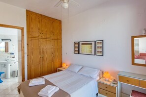 A bedroom with a bed, bedside tables, a nightstand, a mirror, and a wooden wardrobe. - Rouladina Apt 3 (Stalos)