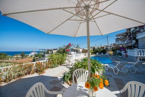 A poolside area with a view of the sea, outdoor seating, and a white umbrella.