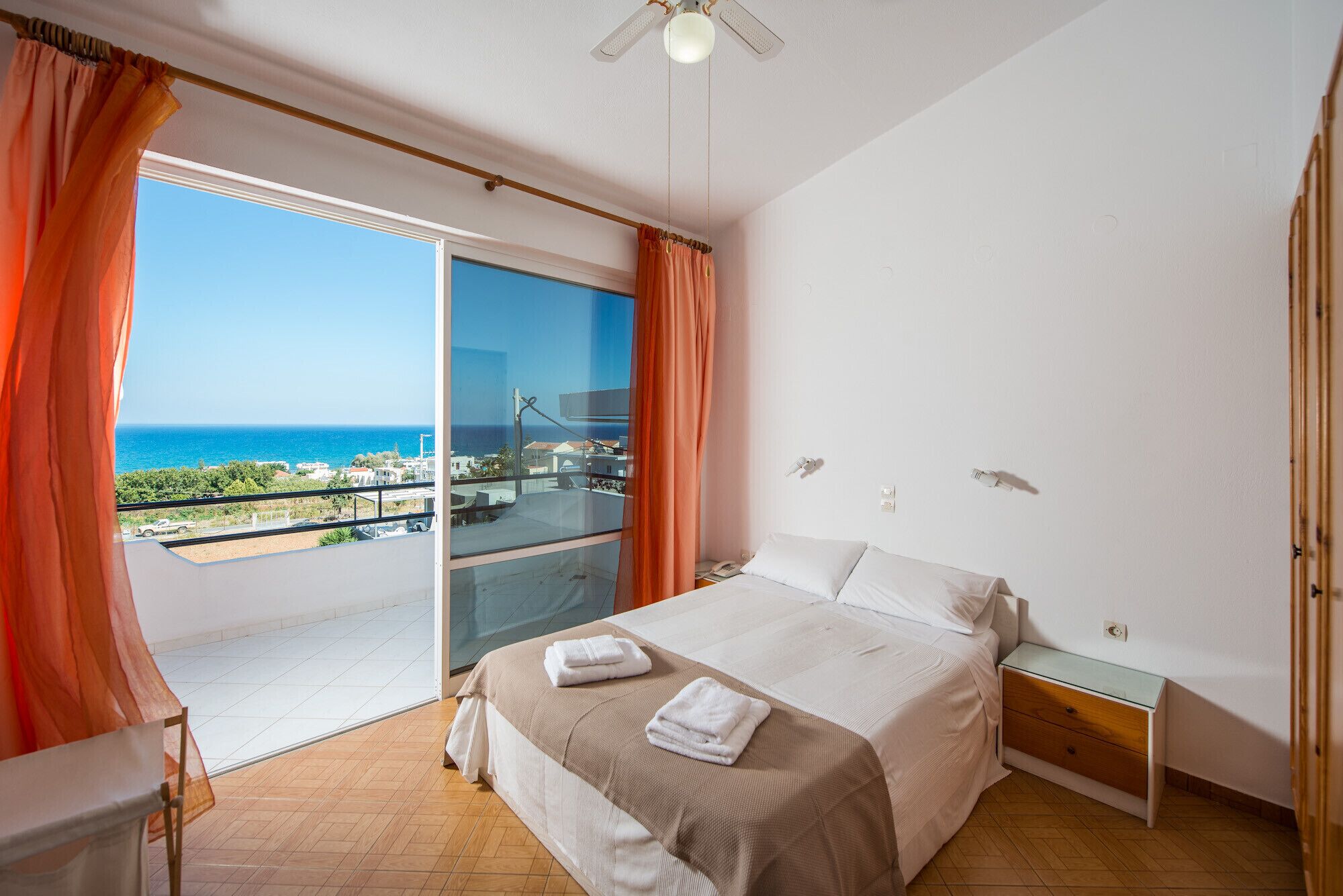 A bedroom with a bed, a nightstand, a glass door leading to a balcony, and a ceiling fan.