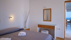 A bedroom with a bed, bedside table, mirror, and a view of the sea through an open door. - Rouladina Apt 6 (Stalos)