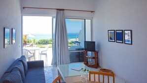 A room with a sofa, a table, a TV, and a view of the sea. - Rouladina Apt 6 (Stalos)