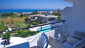 A balcony with a view of the sea, a swimming pool, and modern buildings in the background. - Rouladina Apt 6 (Stalos)
