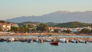 A coastal town with boats docked along the shore, buildings, and mountains in the background. - Villa Afrati (Plaka)