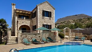 A stone building with a pool, outdoor seating, and a mountain in the background. - Villa Afrati (Plaka)