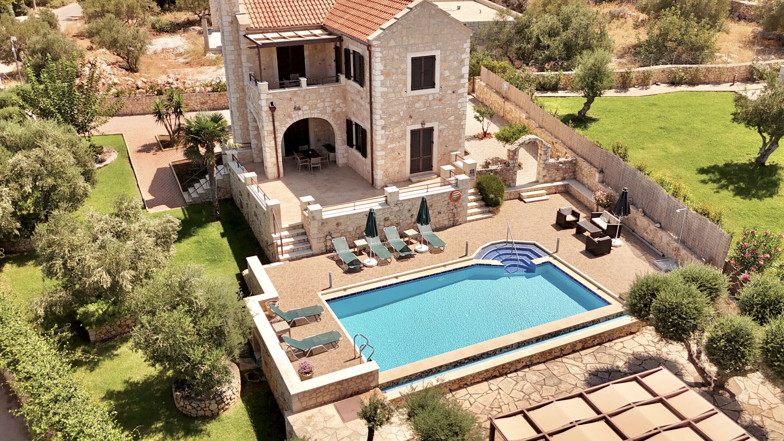 Un edificio de piedra de dos pisos con piscina, mobiliario exterior y un jardín bien cuidado.