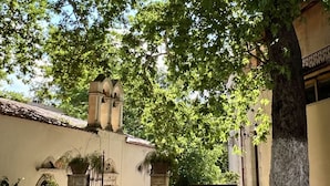 Un edificio con entrada de piedra, techo de tejas y un gran árbol en la fachada.