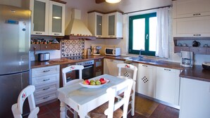 A kitchen with white cabinets, a wooden countertop, a stove, a sink, and a window with green shutters. - Villa Amvrosia (Armeni)