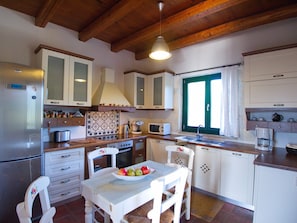 A kitchen with white cabinets, a wooden countertop, a stove, a sink, and a window with green shutters. - Villa Amvrosia (Armeni)