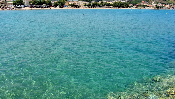 Un pueblo costero con aguas turquesas cristalinas, playa de arena y edificios al fondo.