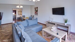 A modern living room with a sectional sofa, a dining area, a flat-screen TV, and a chandelier. - Villa Andreas (Tavronitis)
