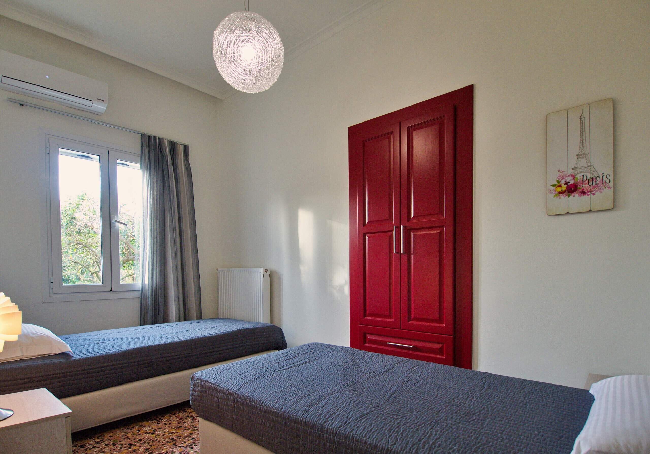 A room with two beds, a red wardrobe, a radiator, a window with curtains, and a wall decoration.