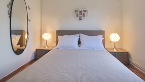 A bedroom with a bed, two bedside lamps, a heart-shaped photo frame, and a mirror on the wall. - Villa Andreas (Tavronitis)