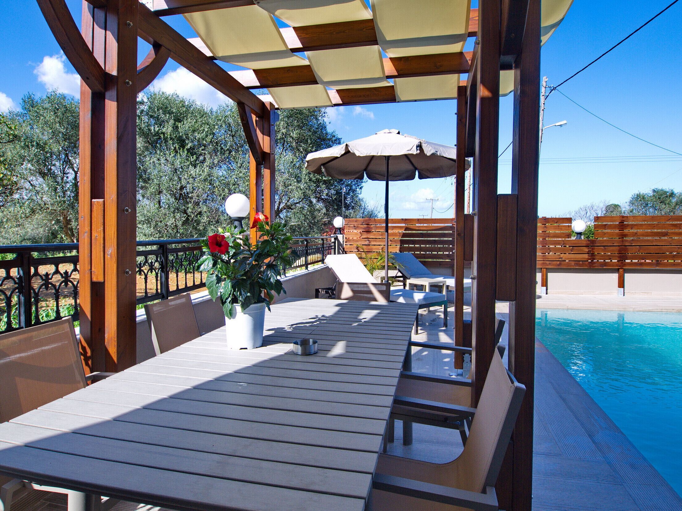 An outdoor pool area with wooden deck seating, umbrellas, and a potted plant.