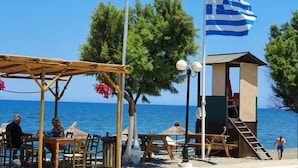 A beachside setting with a lifeguard tower, wooden tables, and chairs under a pergola, overlooking the sea. - Villa Andreas (Tavronitis)