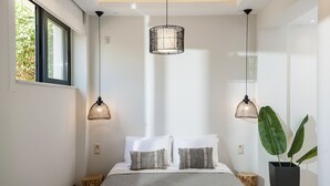 Une chambre moderne avec un grand lit, deux lampes suspendues, une plante en pot et une fenêtre donnant sur un paysage verdoyant.