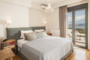 A modern hotel room with a large bed, a nightstand, a table, and a view of the outdoors through a sliding glass door. - Villa Anemi (Sternes)