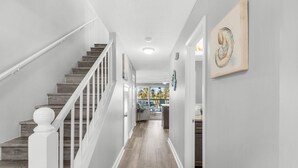Un couloir avec un escalier en bois, des murs blancs et un luminaire au plafond.