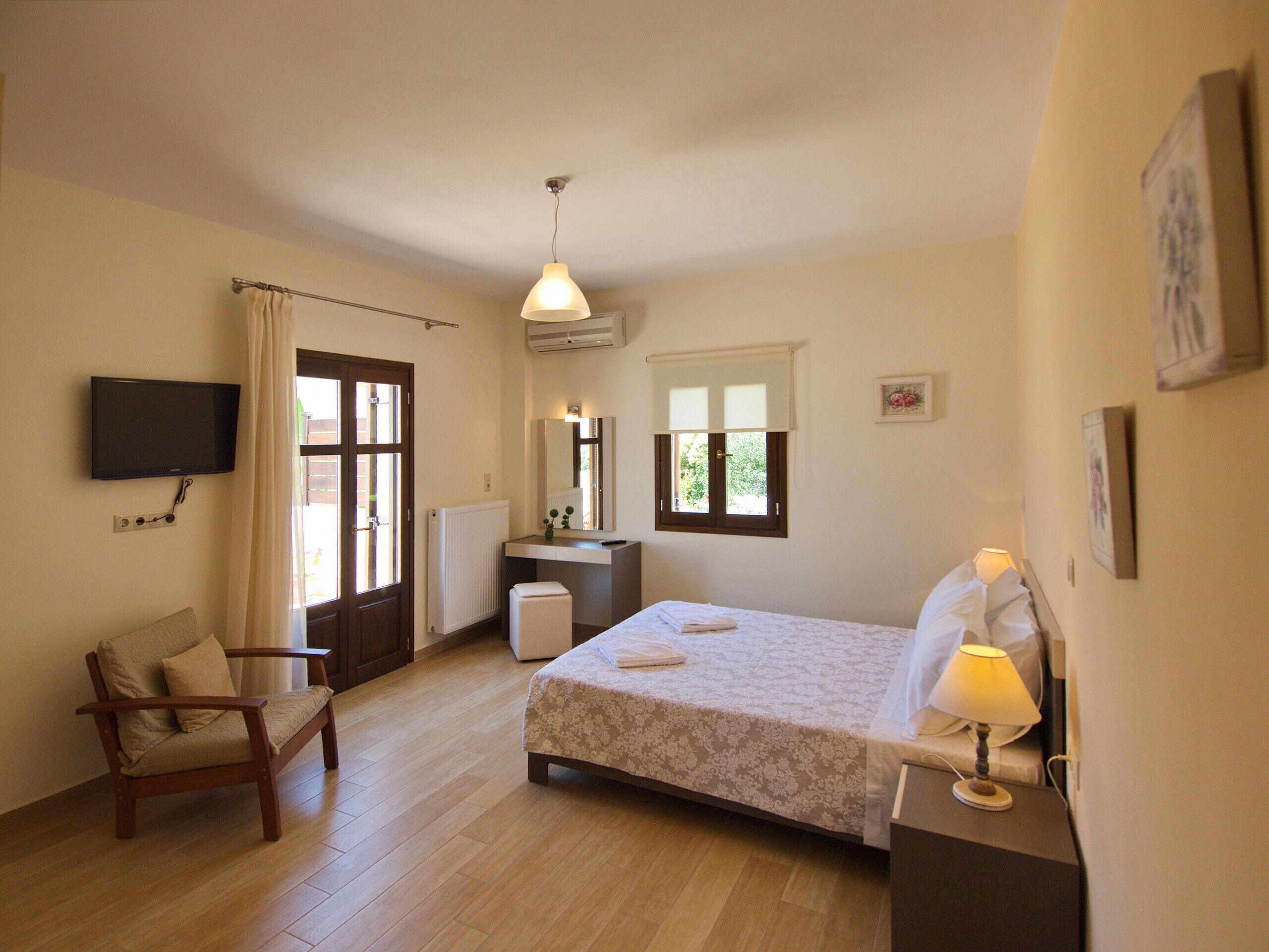 A bedroom with a bed, a chair, a desk, a TV, and a window.