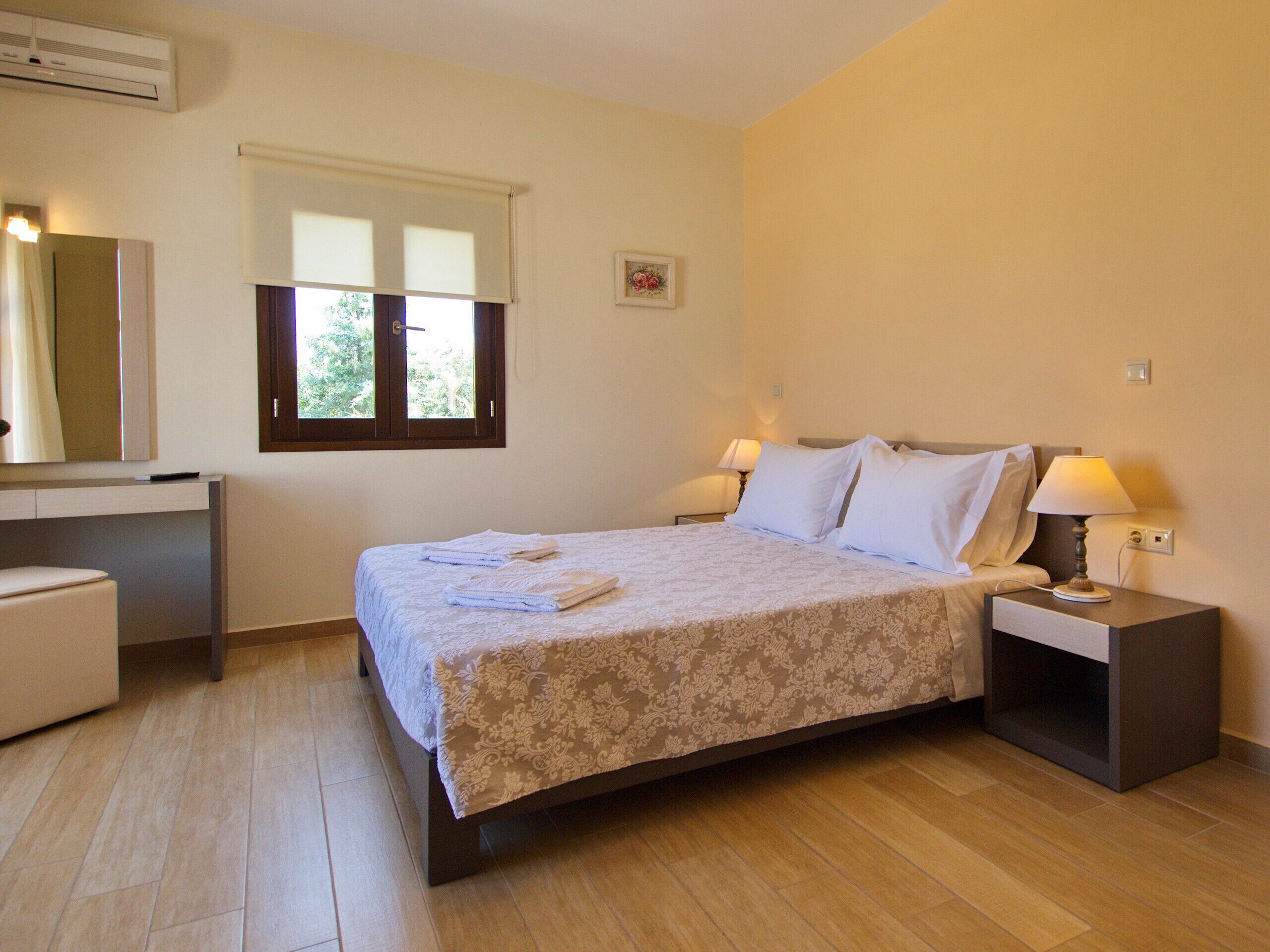 A hotel room with a bed, bedside lamps, a desk, and a window.