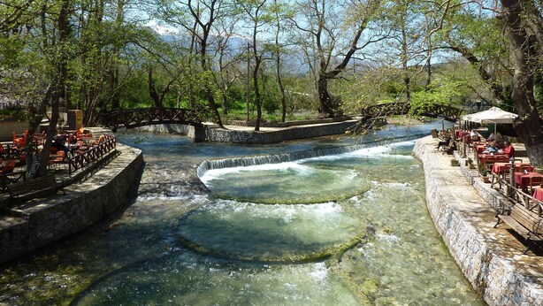 A riverside restaurant with outdoor seating and a stone bridge. - Villa Artemis (Vrises)