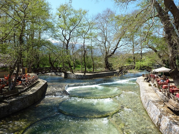 A riverside restaurant with outdoor seating and a stone bridge.