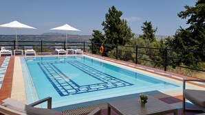 A swimming pool with lounge chairs and umbrellas, surrounded by a railing and trees. - Villa Artemis (Vrises)