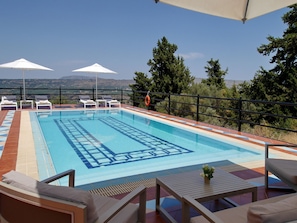 A swimming pool with lounge chairs and umbrellas, surrounded by a railing and trees.
