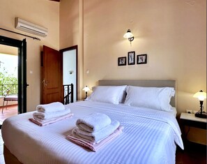 A hotel room with a bed, two bedside lamps, a door, and a wall-mounted air conditioner. - Villa Artemis (Vrises)