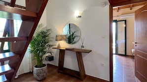 A staircase with wooden railings, a potted plant, a table with a lamp, a mirror, and a door leading to another room. - Villa Artemis (Vrises)