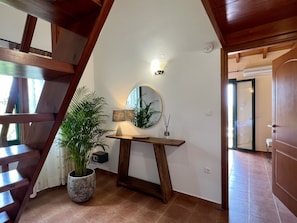 A staircase with wooden railings, a potted plant, a table with a lamp, a mirror, and a door leading to another room.