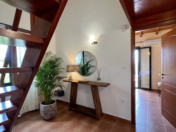 A staircase with wooden railings, a potted plant, a table with a lamp, a mirror, and a door leading to another room.