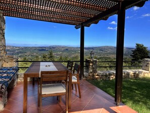 A terrace with a table and chairs, overlooking a mountainous landscape. - Villa Artemis (Vrises)