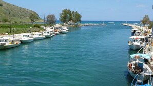 A marina with several boats docked along the shore, a clear sky, and a hilly landscape in the background. - Villa Artemis (Vrises)