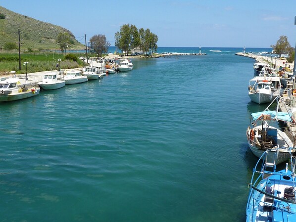 Un port de plaisance où plusieurs bateaux sont amarrés le long de la côte, un ciel dégagé et un paysage vallonné en arrière-plan.