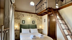 Ein Schlafzimmer mit Steinwand, einer Holztreppe und einem Bett mit weißen Leinen.