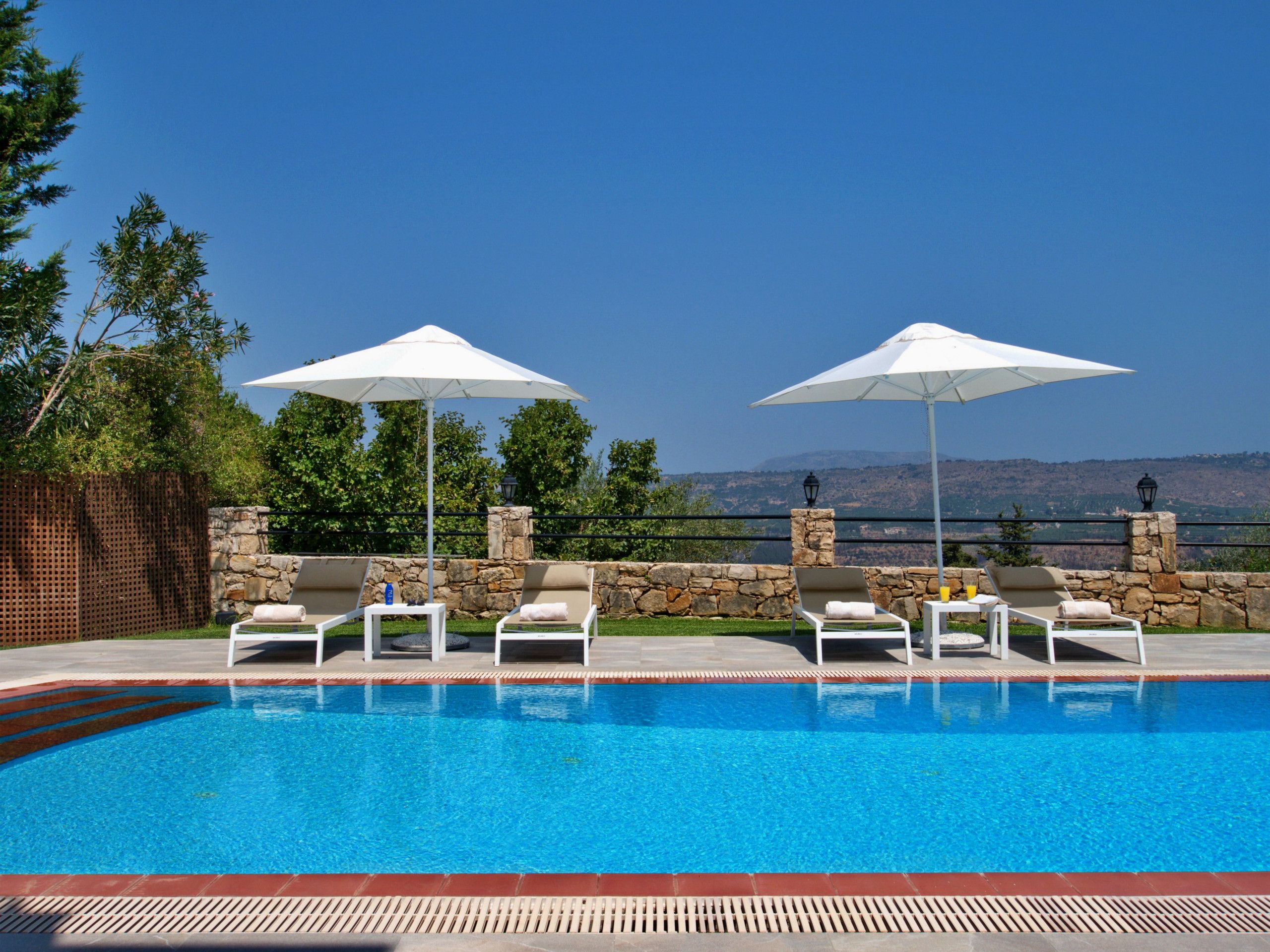 Un espace piscine agrémenté de chaises longues et de parasols, entouré de murs en pierre et offrant une vue sur le paysage.