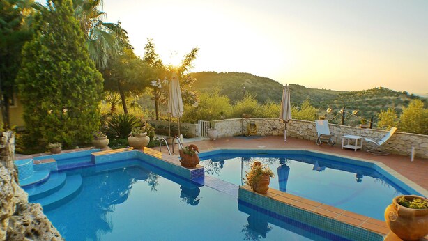 A swimming pool with a stone wall, lounge chairs, and potted plants. - Villa Clio (Stalos)