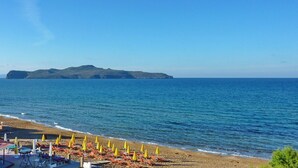 A beach with rows of sun loungers and umbrellas, a clear blue sky, and a distant island. - Villa Clio (Stalos)