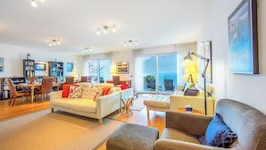 A spacious living area with a dining table, multiple seating options, and large windows offering a view. - Argegno Fronte Lago (Argegno)