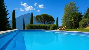 A clear blue swimming pool with two lounge chairs and a mountain in the background. - Villa Isella - Mansarda (Carlazzo)