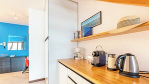 A modern kitchen with a wooden countertop, a coffee maker, a kettle, and a shelf with books and a hat. - Balcone di Noa e Stella (Menaggio)
