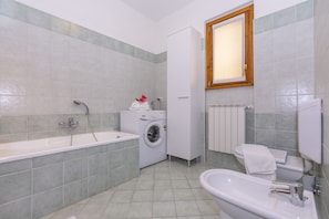 A modern bathroom with a bathtub, a sink, a toilet, and a washing machine.