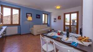 A dining area with a table set for two, a sofa, and a window with a view of a building. - Fontana Del Lago Apt. 16 (Varenna)