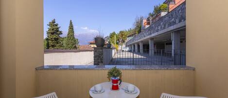 A balcony with two white chairs, a small round table, and a potted plant.