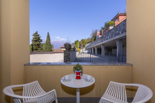 A balcony with two white chairs, a small round table, and a potted plant.