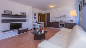A modern living room with a white sofa, a flat-screen TV, a coffee table, and a dining area with a white table and chairs. - Fontana Del Lago Apt. 16 (Varenna)