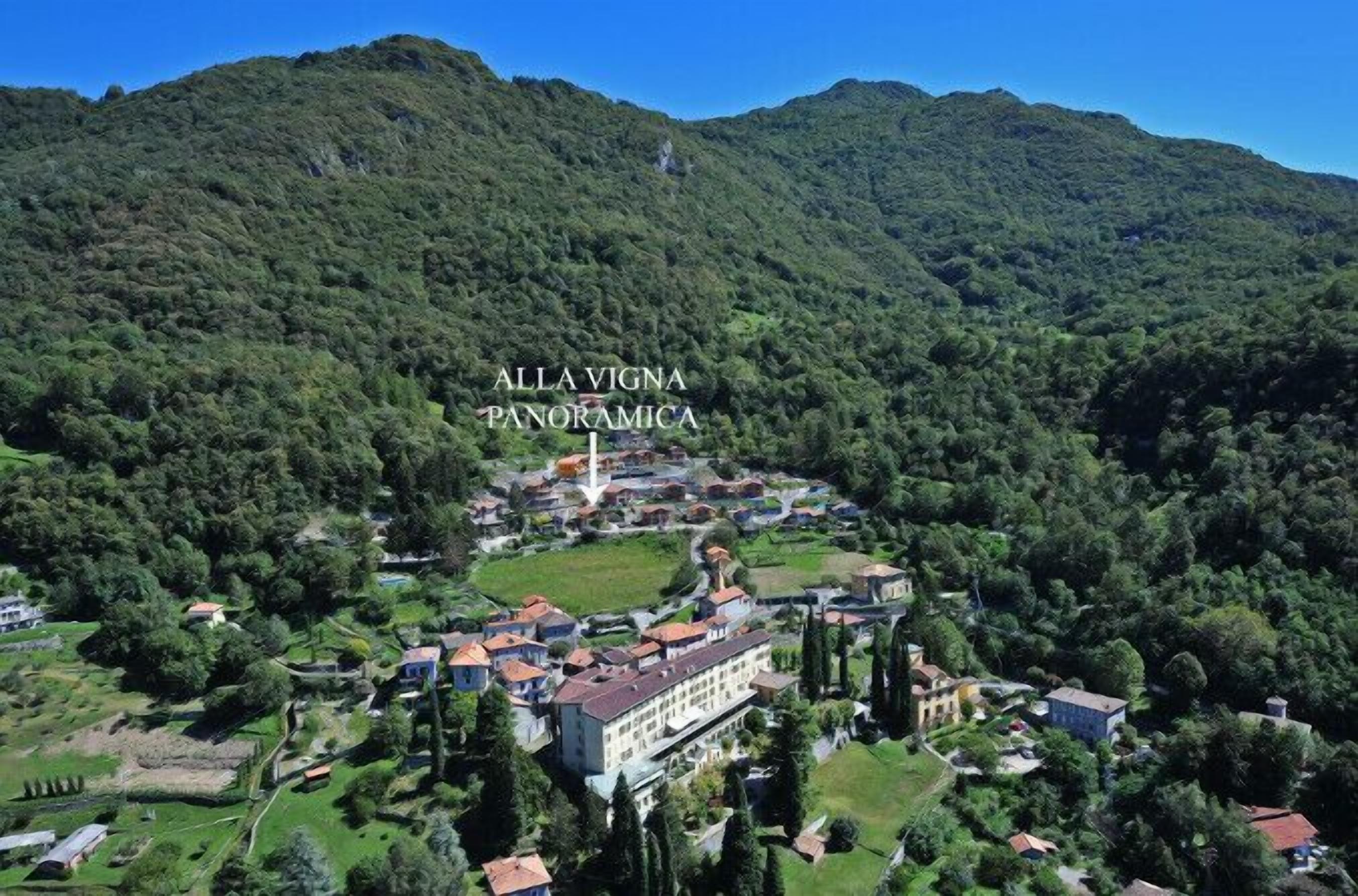 Vista panorámica de Alla Vigna, con un edificio central rodeado de exuberante vegetación y colinas.