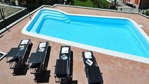 A swimming pool with lounge chairs, surrounded by buildings with red-tiled roofs, set against a backdrop of mountains and a lake. - Alla Vigna Panoramica (Perledo)